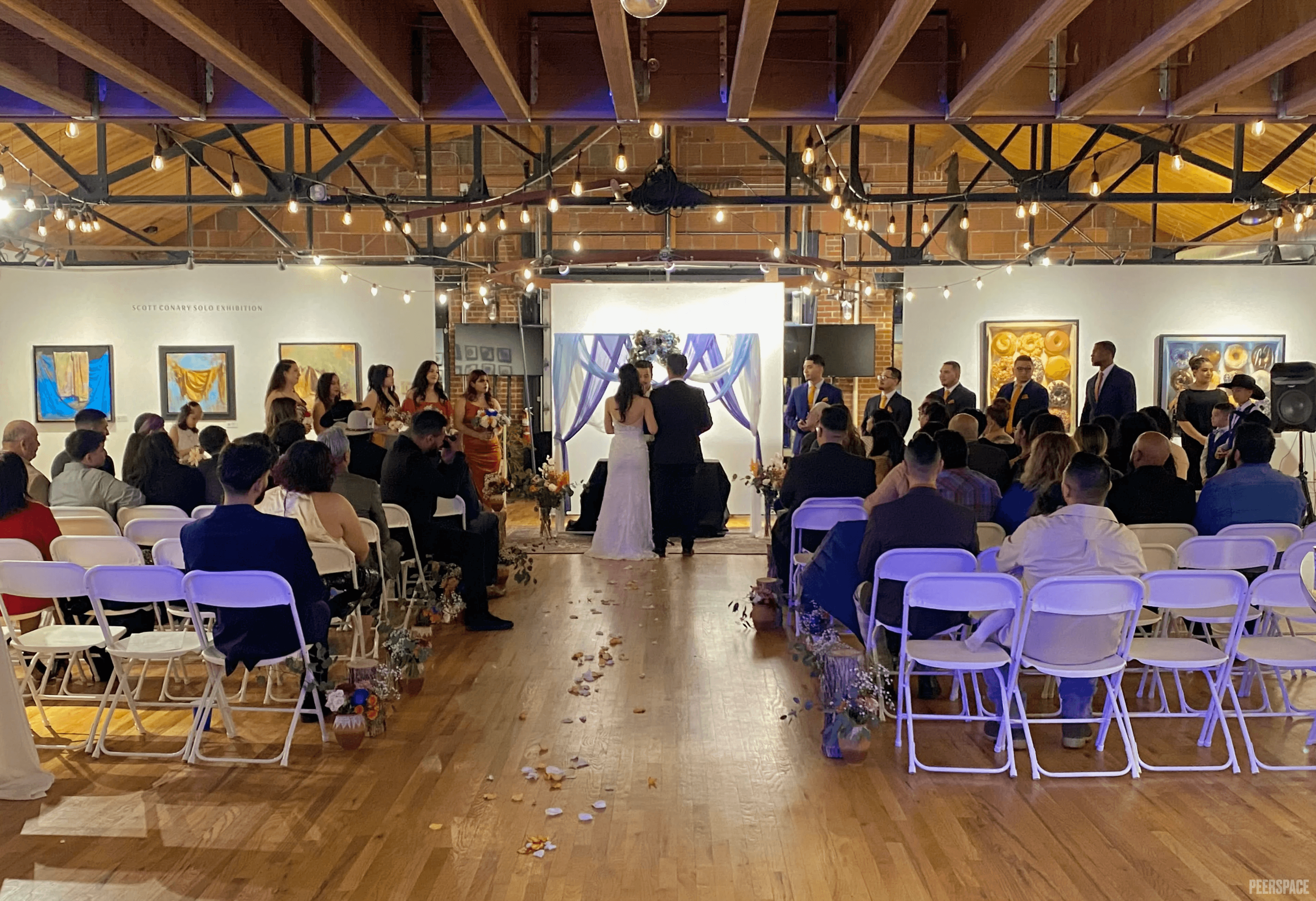 Wedding ceremony in progress at Sterling Event Space, candles down the aisle and string lights overhead